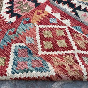 Op de afbeelding: Een close-up van een rood, blauw en beige gestreept tapijt met een witte franje. Het tapijt heeft een geometrisch ontwerp met ingewikkelde details.