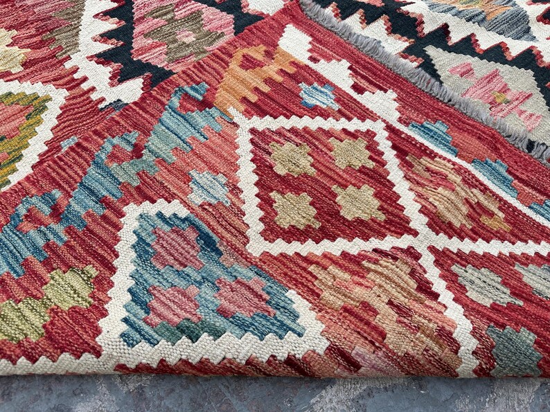Op de afbeelding: Een close-up van een rood, blauw en beige gestreept tapijt met een witte franje. Het tapijt heeft een geometrisch ontwerp met ingewikkelde details.