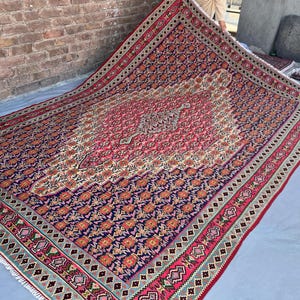 May include: A large rectangular area rug featuring a deep navy blue field covered in repeating orange and pink floral motifs. A central cream-colored medallion with intricate geometric patterns sits in the middle, framed by a wide red border.