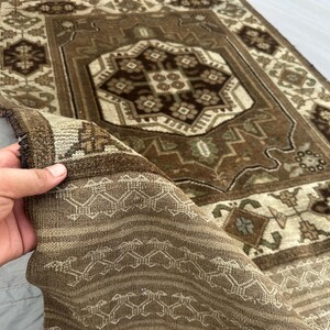 Puede incluir: Una alfombra rectangular marr&oacute;n y beige con un intrincado patr&oacute;n geom&eacute;trico. La alfombra presenta un dise&ntilde;o de medall&oacute;n central y un borde con motivos repetidos. La alfombra est&aacute; hecha de un material tejido y tiene un borde con flecos.