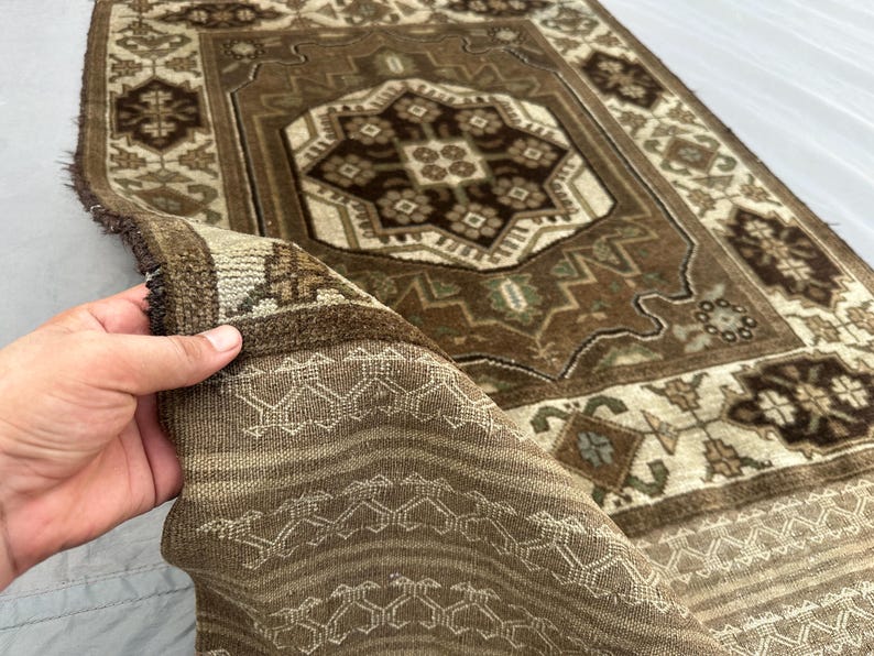 Puede incluir: Una alfombra rectangular marr&oacute;n y beige con un intrincado patr&oacute;n geom&eacute;trico. La alfombra presenta un dise&ntilde;o de medall&oacute;n central y un borde con motivos repetidos. La alfombra est&aacute; hecha de un material tejido y tiene un borde con flecos.