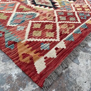 Op de afbeelding: Een rood, oranje en blauw patroonteppich met een franje rand. Het tapijt heeft een geometrisch ontwerp met ruitvormen en ingewikkelde details.