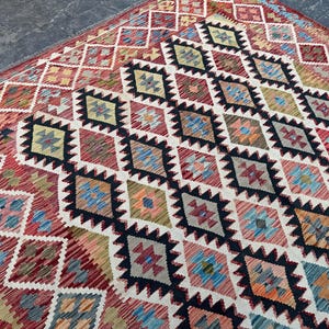 Op de afbeelding: Een kleurrijk tapijt met een ruitpatroon in tinten rood, blauw, groen en wit. Het tapijt heeft een traditioneel ontwerp en is gemaakt van wol.