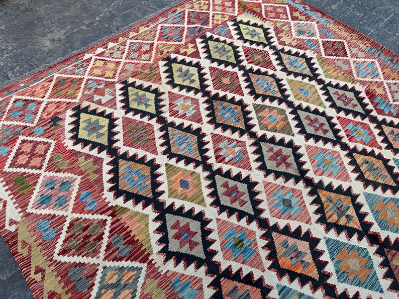 Op de afbeelding: Een kleurrijk tapijt met een ruitpatroon in tinten rood, blauw, groen en wit. Het tapijt heeft een traditioneel ontwerp en is gemaakt van wol.