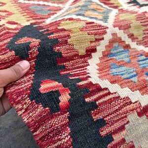 Op de afbeelding: Close-up van een rood, wit en blauw gepatroneerd tapijt met ingewikkelde geweven patronen. Het tapijt heeft een traditionele, handgeweven uitstraling en gevoel.