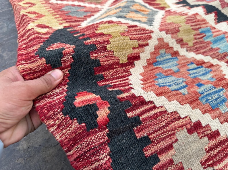 Op de afbeelding: Close-up van een rood, wit en blauw gepatroneerd tapijt met ingewikkelde geweven patronen. Het tapijt heeft een traditionele, handgeweven uitstraling en gevoel.