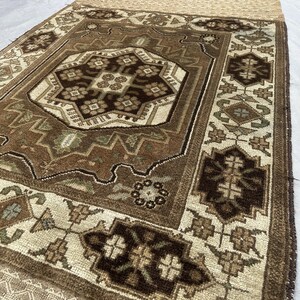 Puede incluir: Una alfombra rectangular con un medall&oacute;n central y dise&ntilde;os de borde intrincados. La alfombra presenta una paleta de colores marr&oacute;n, beige y crema. La alfombra tiene un borde con flecos y patrones geom&eacute;tricos.