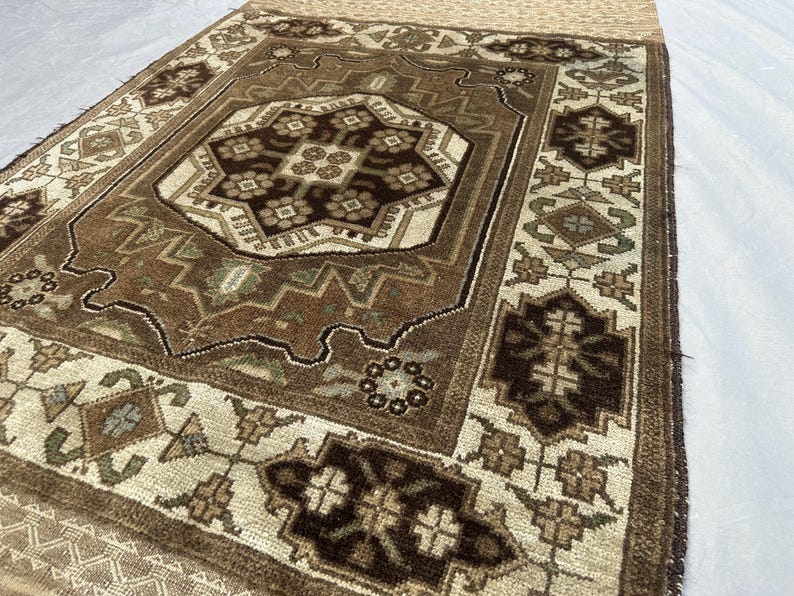 Puede incluir: Una alfombra rectangular con un medall&oacute;n central y dise&ntilde;os de borde intrincados. La alfombra presenta una paleta de colores marr&oacute;n, beige y crema. La alfombra tiene un borde con flecos y patrones geom&eacute;tricos.