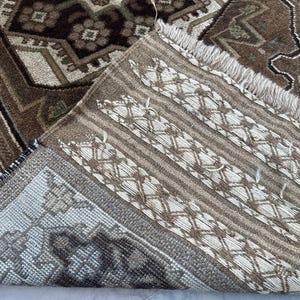 Puede incluir: Primer plano de una alfombra estampada marr&oacute;n y beige. La alfombra presenta un dise&ntilde;o complejo con flecos en un borde. La parte inferior revela un patr&oacute;n contrastante. La paleta de colores incluye marr&oacute;n, beige y gris.