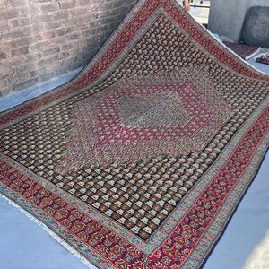 May include: A large rectangular area rug featuring a dark navy blue field covered in a repeating geometric pattern of small light-colored motifs. The rug has a prominent central diamond medallion in shades of red and pink with a wide red border.