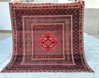 Puede incluir: Una alfombra cuadrada anudada a mano con una paleta de colores rojo intenso y negro con intrincados patrones geométricos. El diseño incluye un motivo central de diamante rodeado por múltiples bordes concéntricos con elementos florales.