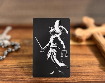 May include: A rectangular black metal card featuring a white graphic illustration of a winged angel figure holding a sword in one hand and a set of scales in the other. The design is centered on the front surface of the flat, thin card.