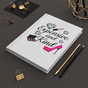 May include: White journal featuring the text "Expensive and Kind" with illustrations of diamonds, lipstick, a makeup palette, and a high heel. Gold and black pencils and gold binder clips are also visible.