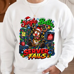 May include: A white crewneck sweatshirt featuring a graphic of a reindeer wearing a Santa hat and scarf, tangled in colourful holiday lights among server racks. The text reads Jingle Bells, SERVER FAILS, 404 JOY NOT FOUND, and SERVER ERROR.