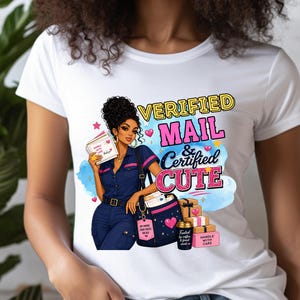 以下が含まれることがあります： 白いTシャツ。郵便配達員のグラフィックと「Verified Mail & Certified Cute」の文字。イラストには、郵便バッグ、小包、ハートが含まれています。郵便配達員は青い制服を着ています。