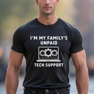 May include: Black t-shirt with white text that reads "I'M MY FAMILY'S UNPAID TECH SUPPORT." The graphic includes a laptop with gear icons. The shirt is short-sleeved and made of a soft material.