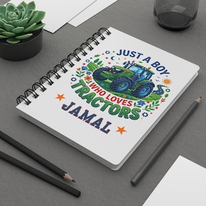 May include: A white spiral-bound notebook featuring a graphic of a green tractor in a field. The text reads JUST A BOY WHO LOVES TRACTORS and the name JAMAL. The design includes colorful flowers, stars, and sun icons surrounding the tractor illustration.