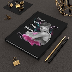 Può includere: Diario nero con la scritta "Short Hair, Strong Woman" e un'illustrazione di una donna con i capelli corti. La copertina presenta accenti rosa e turchese. Sono visibili anche matite dorate e nere e fermagli dorati.
