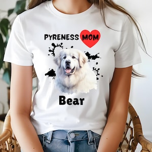 Puede incluir: Camiseta blanca con texto negro que dice "Pyrenees Mom" con un corazón rojo y un perro Great Pyrenees blanco con manchas negras en el fondo. El nombre del perro es "Bear" en texto negro.