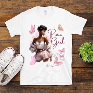 May include: White t-shirt featuring a digital illustration of a woman in pink shorts and a jacket, with butterflies and the text "Pixie Girl". A pair of white Converse sneakers are visible on the left.