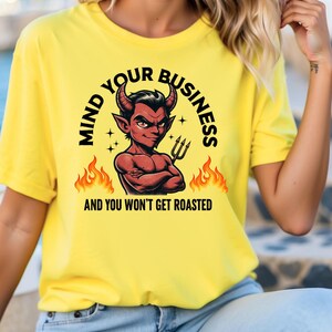 May include: Yellow t-shirt featuring a red devil cartoon graphic and the text "Mind Your Business and You Won't Get Roasted".