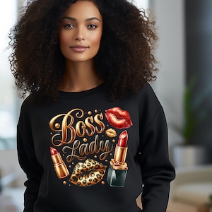 May include: Black sweatshirt with a gold and red design featuring the words "Boss Lady", red lipstick, and leopard print lips. The design is embellished with gold accents. The sweatshirt is a crew neck style.