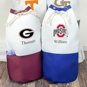 May include: Four white drawstring bags with team logos and names. Each bag has a colored bottom and trim. The logos include a "T", "GT", "G", and "Ohio State" emblem. The names "Thomas" and "William" are printed on the bags.