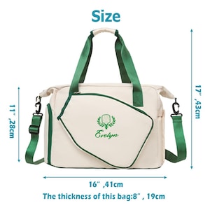 Op de afbeelding: Cr&egrave;mekleurige draagtas met groene accenten, handvatten en schouderriem. De tas heeft een geborduurd embleem en de naam "Evelyn". Afmetingen: 41 cm breed, 28 cm hoog, 43 cm diep en 19 cm dik.