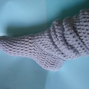 May include: A pair of gray crocheted socks with a ribbed cuff. The socks are made with a simple stitch pattern and have a soft, cozy look.