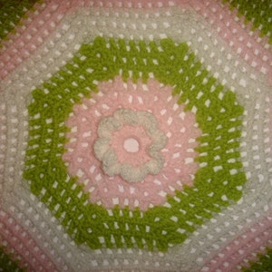 May include: A crocheted hexagon blanket with a pink, green, and white color scheme. The center of the blanket features a large white flower.
