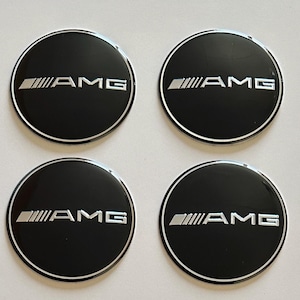 Puede incluir: Cuatro tapacubos AMG negros con el logotipo AMG plateado. Las tapas son redondas con un borde plateado. El logotipo AMG es plateado y presenta el emblema AMG y las letras "AMG".