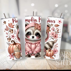 May include: White tumbler featuring a cute raccoon in a pink hoodie, surrounded by pumpkins, flowers, and fall leaves. The text "Pumpkin Kisses" is displayed on the tumbler. A fall-themed drink is also shown.