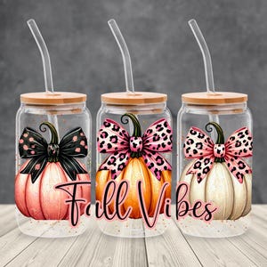Op de afbeelding: Drie glazen bekers met bamboe deksels en doorzichtige rietjes. Elke beker heeft een pompoenontwerp met een strik. De pompoenen zijn in tinten oranje, roze en crème. De tekst "Fall Vibes" staat op de voorkant.