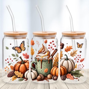 May include: Three glass tumblers with bamboo lids and clear straws. Each tumbler features a fall-themed design with pumpkins, leaves, acorns, and butterflies. One has a coffee design. The tumblers are on a wooden surface.