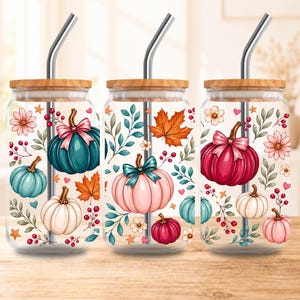 May include: Three clear glass tumblers with bamboo lids and metal straws, each featuring a colorful autumn-themed print of pumpkins, fall leaves, berries, and small flowers in shades of teal, pink, red, and white against a transparent background.