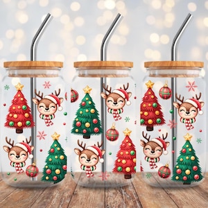Könnte beinhalten: Drei transparente Glasbecher mit Bambusdeckeln und Edelstahlstrohhalmen. Jeder Becher hat ein Weihnachtsdesign mit einem Rentier mit Weihnachtsmütze und Schal, Weihnachtsbäumen und Ornamenten. Die Becher stehen auf einer Holzoberfläche.