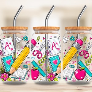 Peut inclure: Trois verres transparents avec couvercles en bambou et pailles en métal, chacun arborant un motif scolaire coloré composé de crayons jaunes, pommes roses, cahiers avec notes A+, ciseaux, règles et petites fleurs sur une surface transparente.