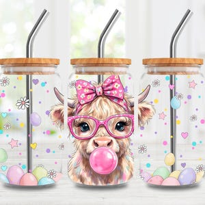 May include: Three glass tumblers with bamboo lids and stainless steel straws. Each tumbler features a whimsical illustration of a Highland cow wearing pink glasses and a bow, blowing a bubble. Decorated with pastel Easter eggs and floral accents.