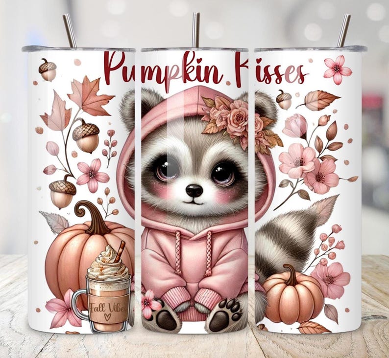 May include: A white tumbler with a fall theme. It features a raccoon wearing a pink hoodie, the text "Pumpkin Kisses", pumpkins, acorns, and floral accents. A coffee cup with the text "Fall Vibe" is also visible.
