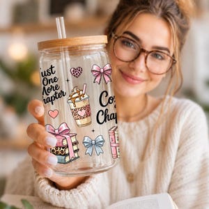 May include: A clear glass tumbler with a wooden lid and straw, decorated with pink bows, hearts, and coffee cup graphics. The tumbler has the text "Just One More Chapter" and "Coffee Chapter".