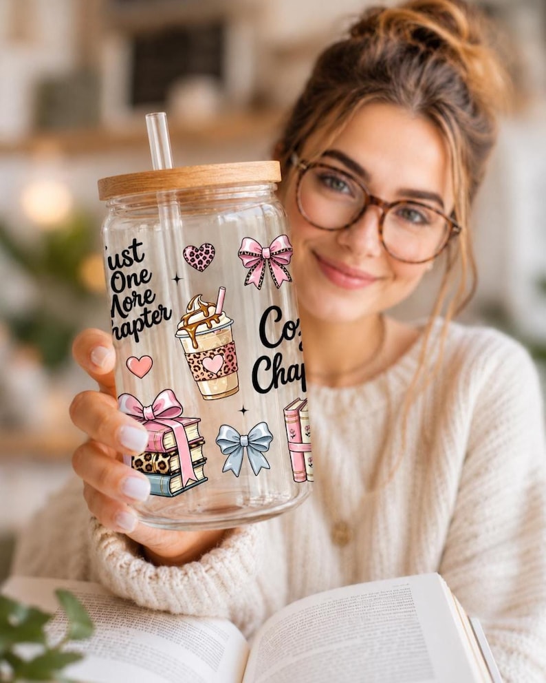 May include: A clear glass tumbler with a wooden lid and straw, decorated with pink bows, hearts, and coffee cup graphics. The tumbler has the text "Just One More Chapter" and "Coffee Chapter".