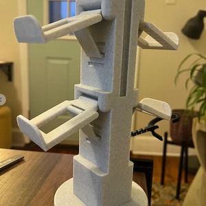 May include: A white 3D printed phone stand with four adjustable arms. The stand has a round base and a square column.
