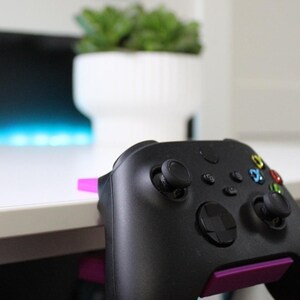 May include: A black video game controller with purple accents. The controller is resting on a white surface.