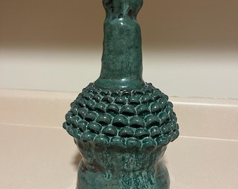 Może przedstawiać: Zielony ceramiczny wazon z fakturowaną, bulwiastą podstawą i wąską szyjką. Wazon ma pstrokaty, postarzany wygląd.