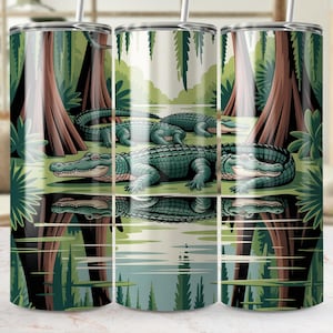 Puede incluir: Un vaso de acero inoxidable con una ilustración de caimanes en un entorno pantanoso. El diseño incluye caimanes verdes, árboles marrones y una superficie de agua reflectante. El vaso tiene una pajita plateada.
