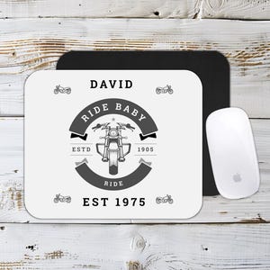 May include: A white mouse mat featuring a motorcycle design and the words "RIDE BABY" and "EST 1975". A black mousepad and a white computer mouse are also visible.