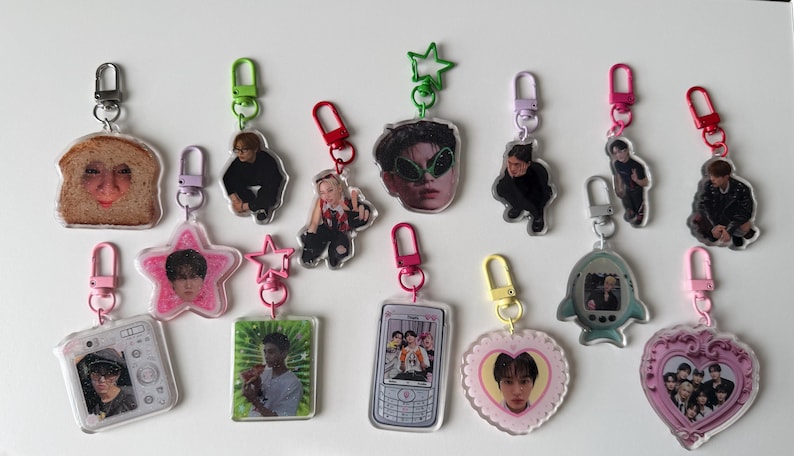 May include: A collection of thirteen acrylic keychains featuring various shapes including a slice of bread, stars, hearts, a camera, a mobile phone, and a fish, each with a colourful clasp and printed with photographic images of people.