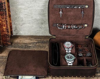 May include: Open brown leather travel jewelry case with a zipper, holding watches, rings, earrings, and a wallet. A separate matching pouch with a zipper is open, revealing a passport and cash.