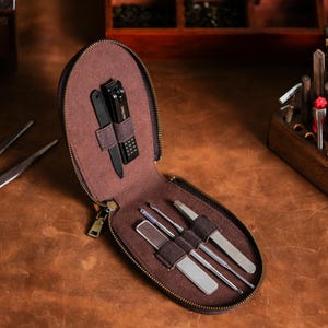 May include: A brown zippered manicure kit with a variety of grooming tools. The kit includes a nail clipper, nail file, and several stainless steel tools. The interior is lined with brown fabric, and the tools are held in place with elastic straps.