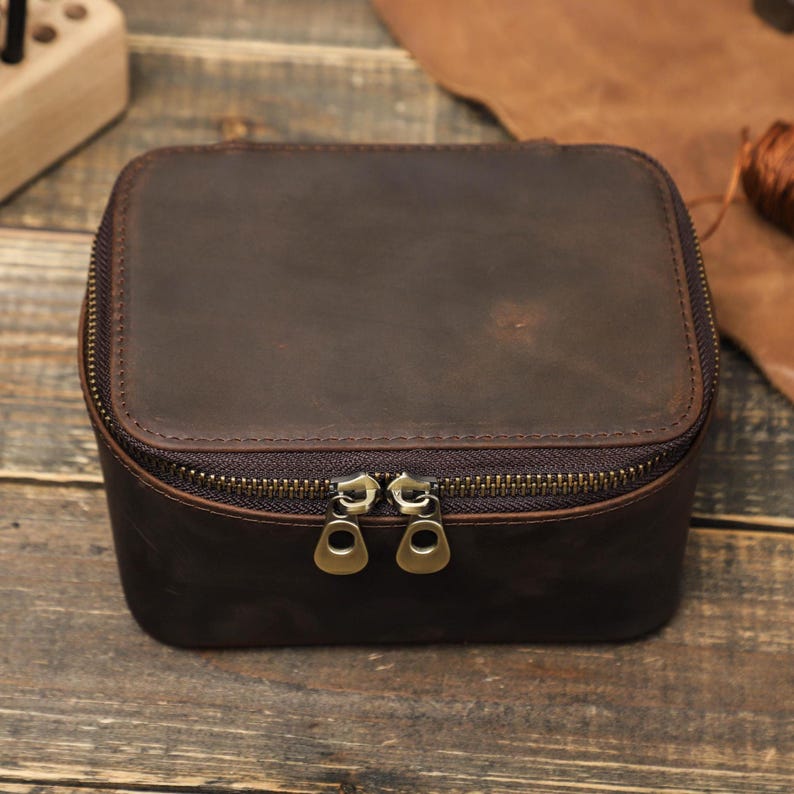 May include: A brown leather zippered travel case with two gold zippers. The case is on a wooden surface.